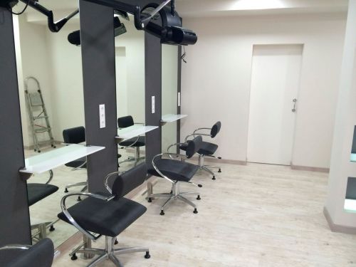 Imagen de varios sillones de peluquería con espejos a la izquierda y pared blanca al frente