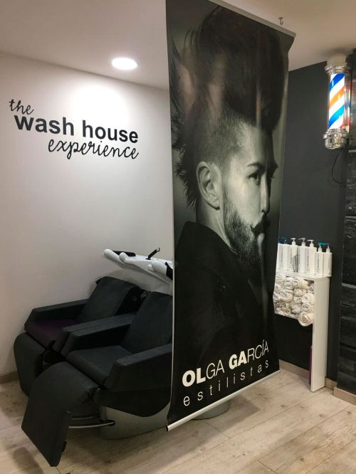 Espacio de lavado con rótulo de The wash house experience separado con lona con imagen de peinado masculino