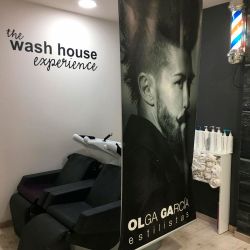 Espacio de lavado con rótulo de The wash house experience separado con lona con imagen de peinado masculino